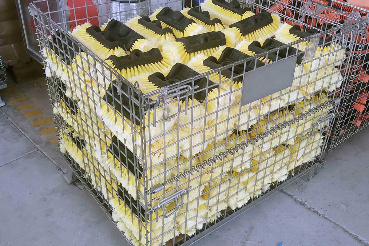 Wire-cage storage bins packed with finished yellow and orange cleaning brush heads